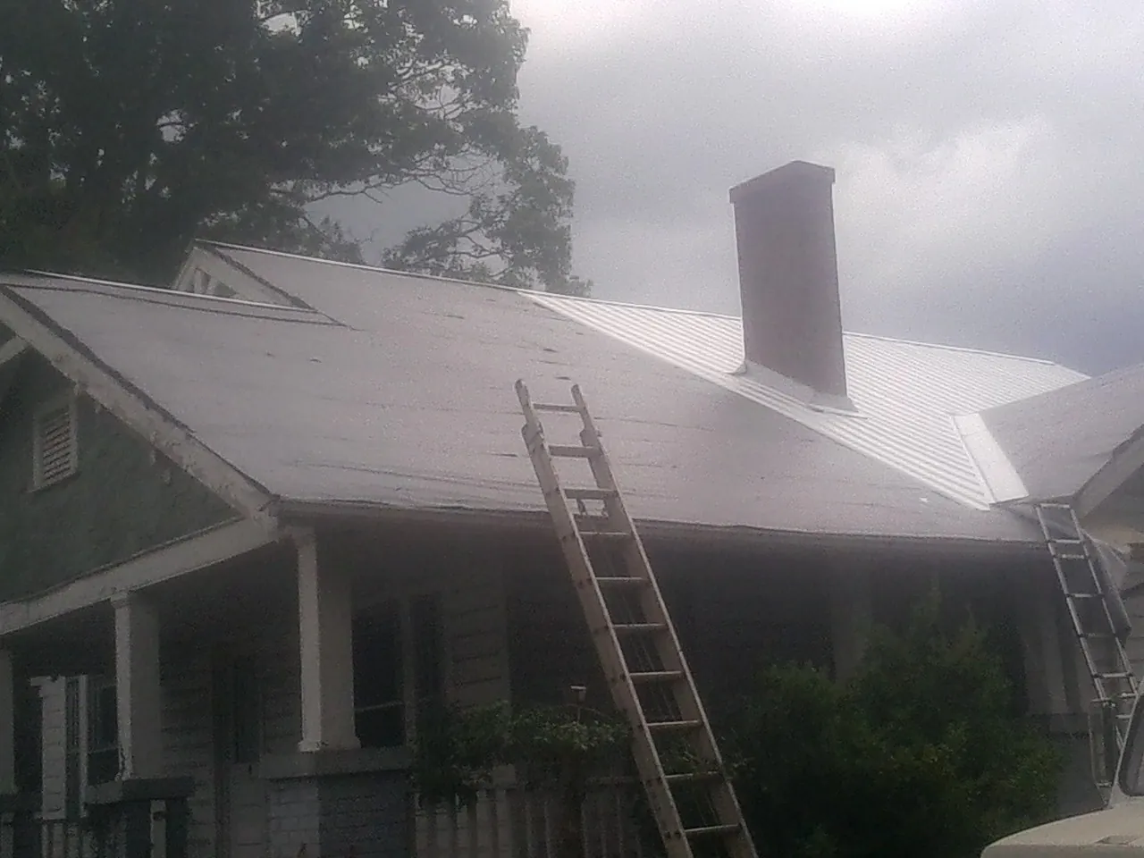 Ladders against a metal roof on an older home with a brick chimney in Raymond