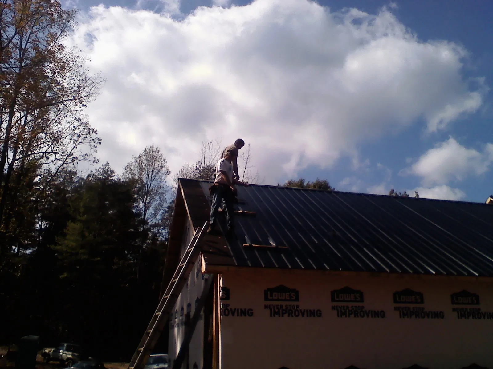 Roofer fastening dark metal panels high against a cloudy sky, from a Roof Inspection job in Raymond